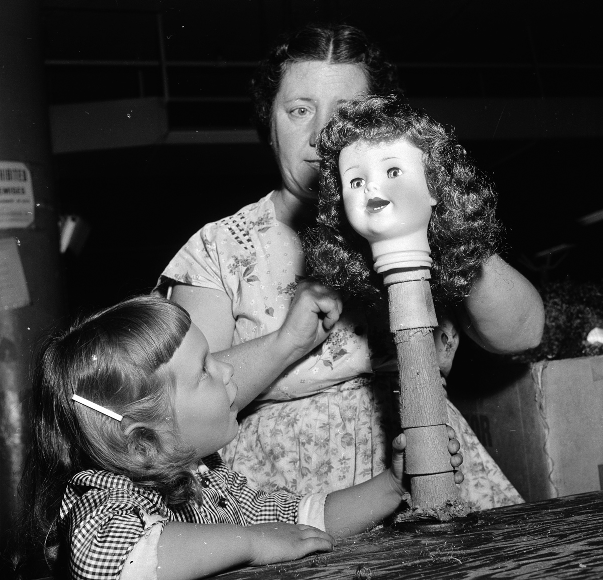 circa 1955: A young girl watching a worker putting hair on a doll's head at the Ideal Toy Company in Jamaica, Long Island, USA. The company is one of the largest toy manufacturers in the world. (Photo by Orlando /Three Lions/Getty Images)
