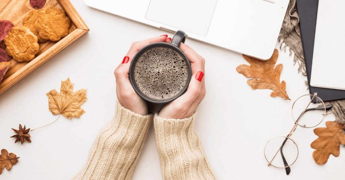 dłonie trzymające kubek kawy na jesiennym biurku